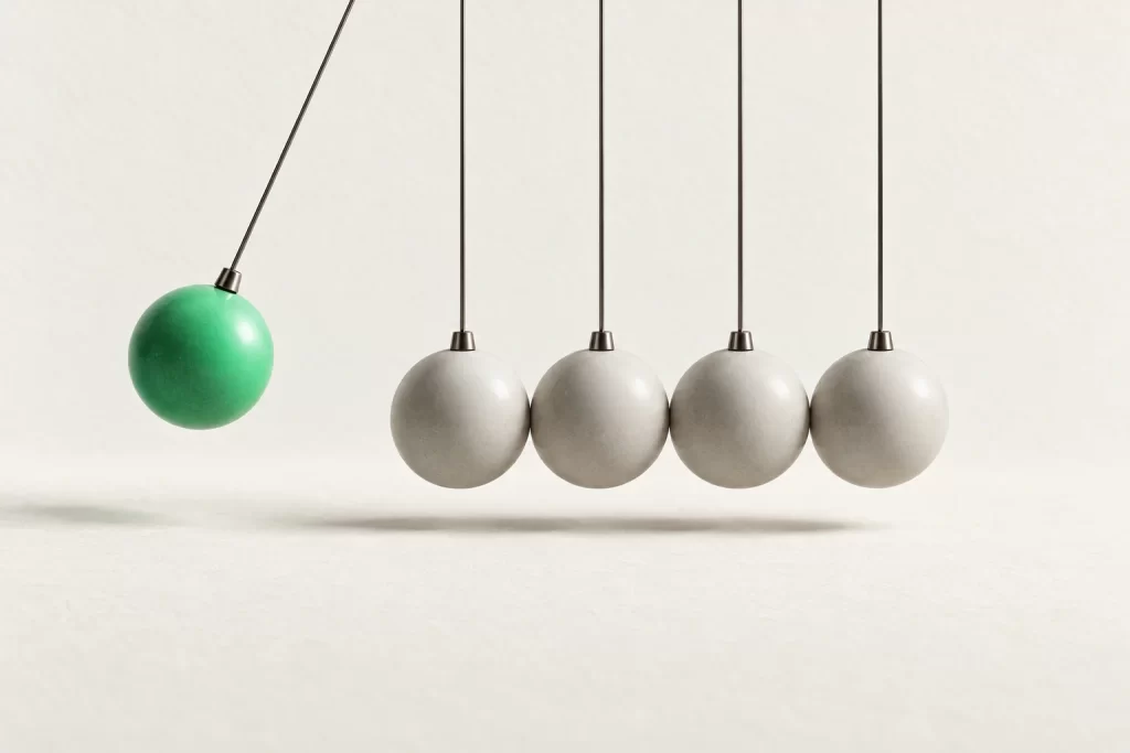 A row of hanging spheres, one green sphere lifted mid-swing